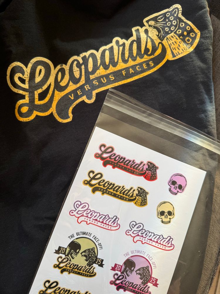 Black tee shirt with the slogan “Leopards versus Faces” and a picture of a roaring leopards face in gold.  An assortment of stickers in black, gold, pink, purple and red—some of the same slogan, some with a picture of a skeleton and the leopard face facing off with the words “The Ultimate Face Off 2025” over them