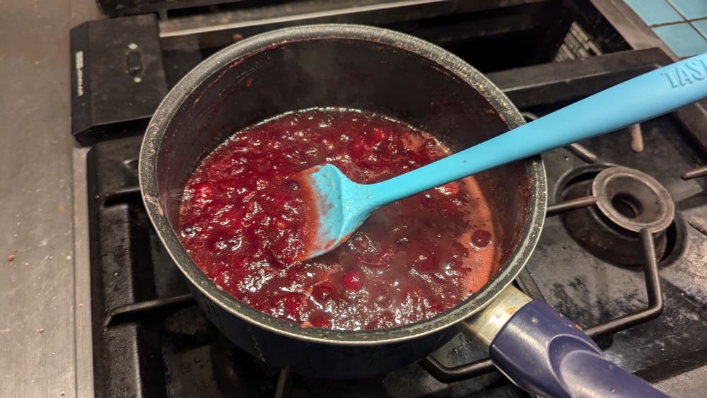 A pot of cranberry sauce, being cooked on a gas range.
