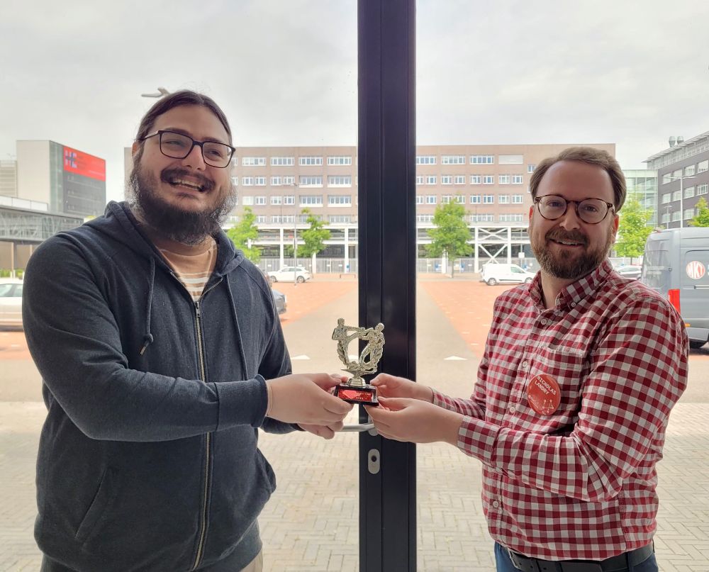 A delightfully nerdy photo of @arash.network receiving a small karate club trophy from @nwlandry.bsky.social