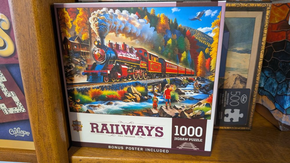 A 1000 piece puzzle by morally vacant company "Master Pieces" a fake ass red steam locomotive with a baffling 6-10-0T wheel arrangement pulls a bad consist of 4 coaches with off kilter perspective past a log cabin in a hallucinatory landscape in which every piece of flora is capable of colorful fall foliage because fuck any sort of semblance of joy in how nature functions. 