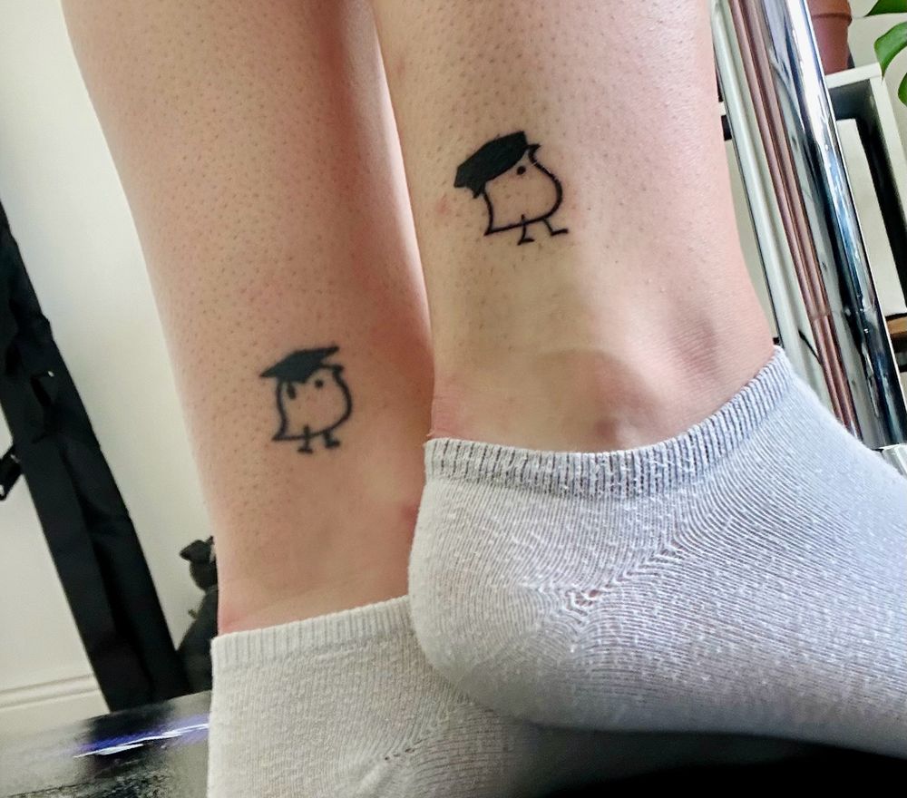 Two small ankle tattoos one on each ankle. The first is a wug wearing a mortarboard. The second newer looking tattoo is a wug wearing a doctoral tam. 