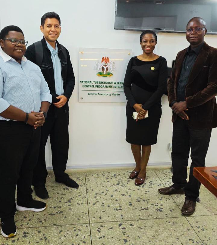 4 people standing in a semi circle smiling and looking towards the camera. sign in the middle stating 'national tuberculoisis & leprosy control programme (NTBLCP) Federal Ministry of Health'