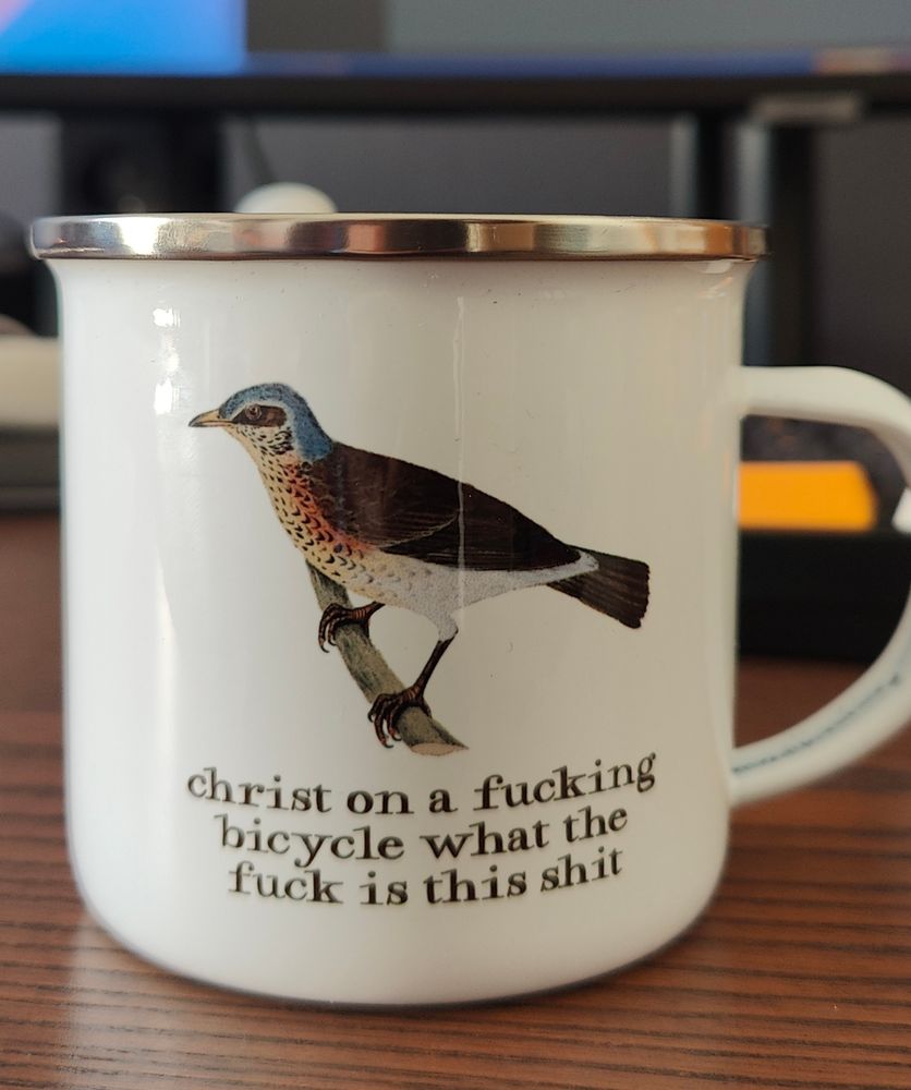 Es una taza esmaltada con el texto: Christ on a fucking bicycle what the fuck is this shit