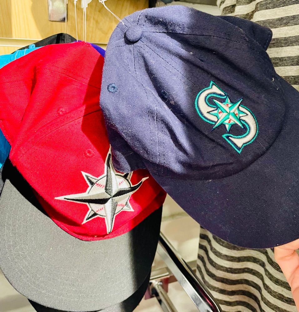 Two Seattle mariners baseball hats. One is red and grey and the other is all blue.