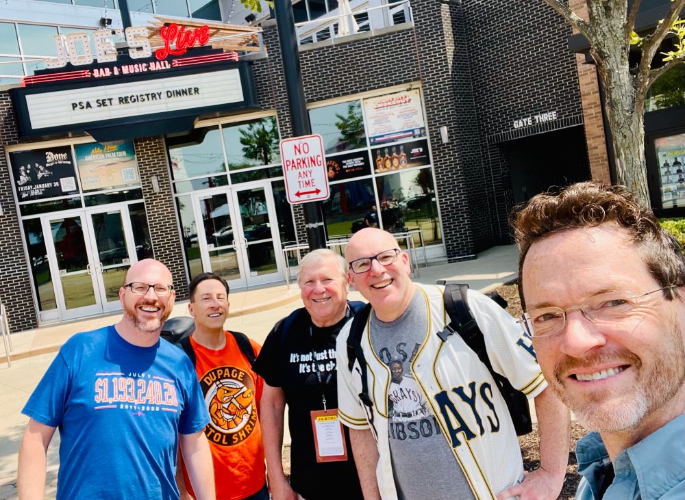 Five men standing in front of a restaurant marquee that says “PSA SET REGISTRY DINNER”