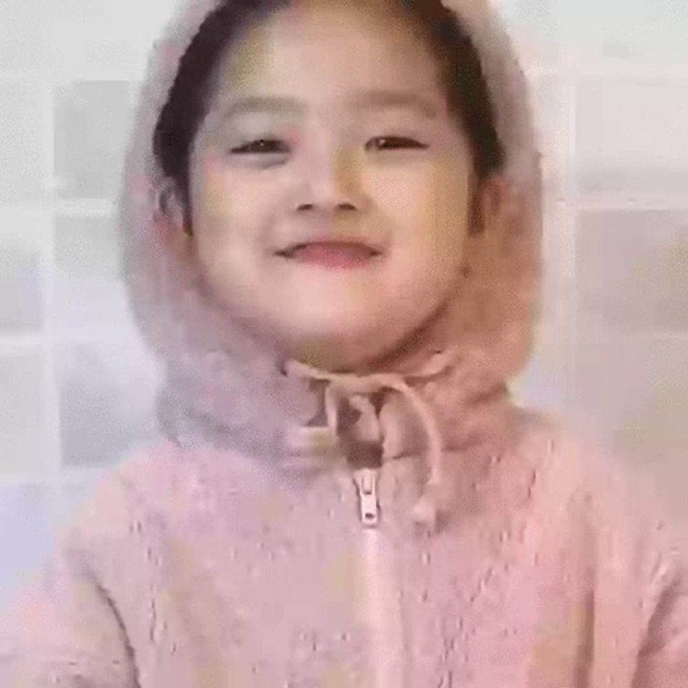 a little girl wearing a pink jacket with a hood is making a funny face .