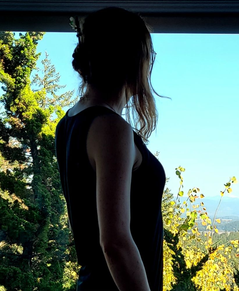 candid photo of a femme woman silhouetted against a large window with a view of nature