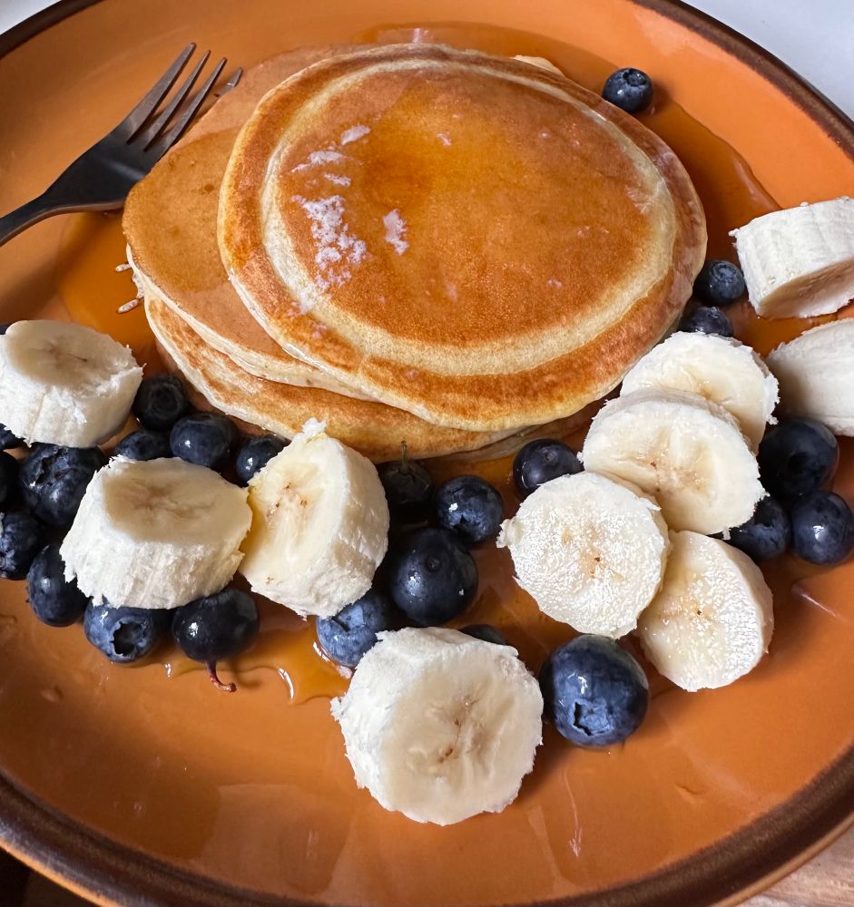 A photograph of a brown China plate. An old plate - my parents bought this set back in the 1970s in Japan. On the plate is some good food! A pile of American style pancakes covered in butter and maple syrup. Next to them are blueberries and a cut up banana. 