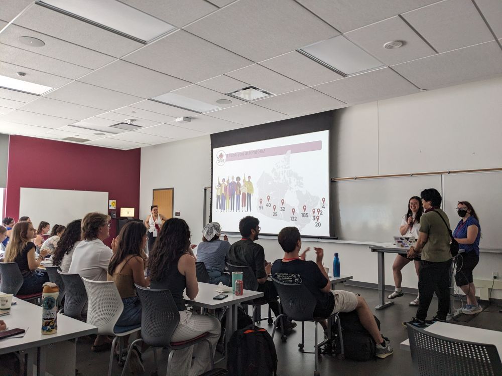 A crowd of people facing a screen and three presenters. The screen shows a group of cartoon people and a map of Canada showing attendees across the country. The header reads "Thank you Attendees!"