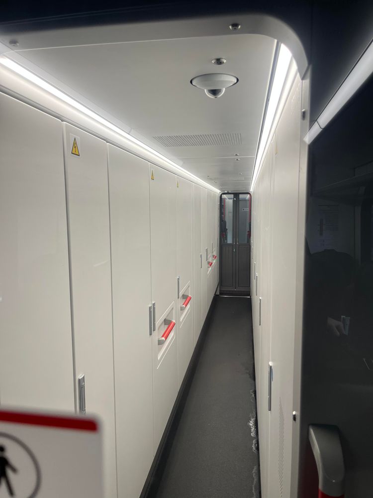The enclosed passageway through the short battery coach, with no windows just a bank of white doors and strip lights in the ceiling.