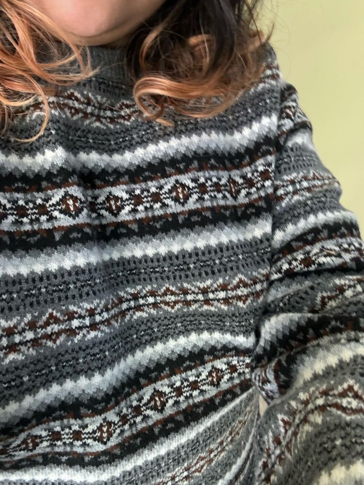a close up of an oversized knitted sweater with a tight color work pattern  in gray black white and brown colors