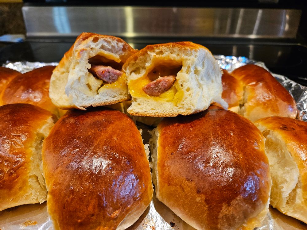 Tray of klobasneks with one cut in half showing sausage and cheese filling baked inside bread