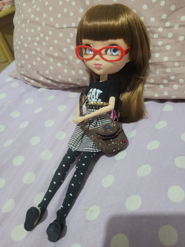 Idem anterior, mas está sentada e de óculos segurando a alça da bolsa 