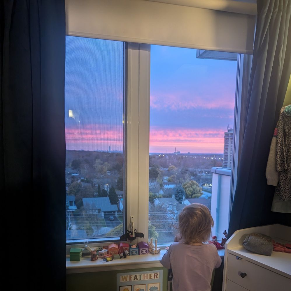 Toddler looking out window to see purple and pink sunrise.