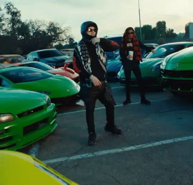 a man in a mask is standing in a parking lot surrounded by green cars .