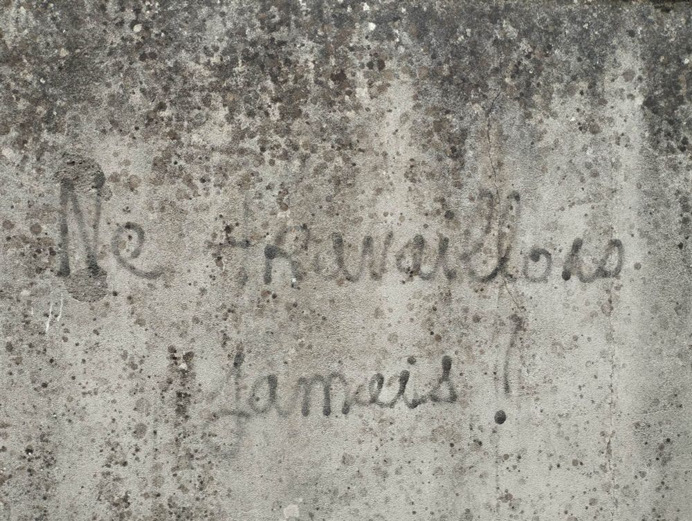 Graffiti très ancien sur un mur en pierre où il est écrit en noir "Ne travaillons jamais !" En lettres cursives