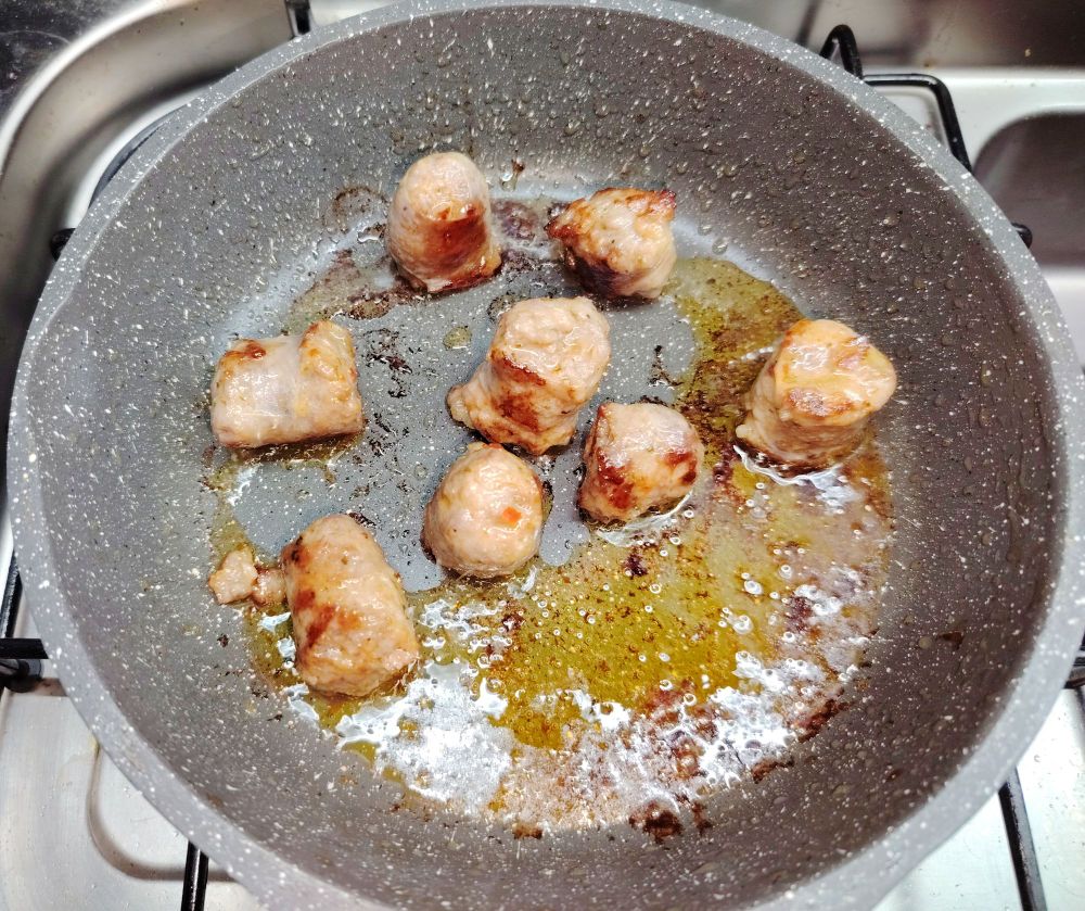 Chunks of pork sausage caramelising in a frying pan