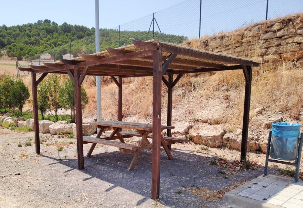 Shaded bench and picnic table at Área de Autocaravanas de Astudillo. 