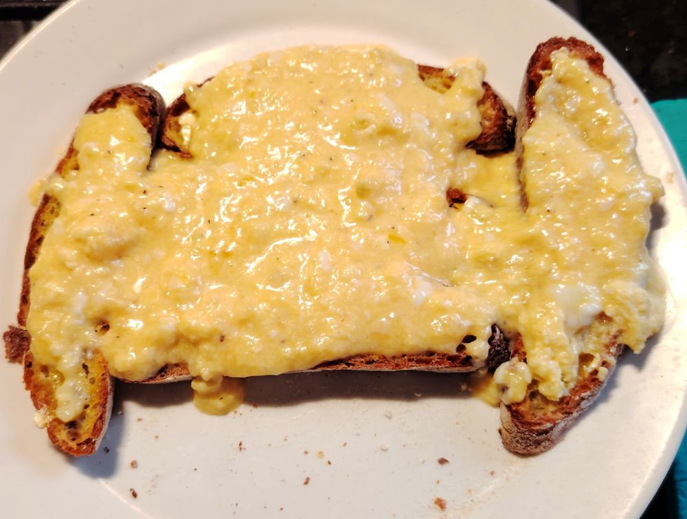 Slices of toasted sourdough topped with creamy scrambled eggs made with extra mature cheddar, served on a white plate with a few crumbs. A rich, comforting twist on Welsh Rarebit, blending bold flavour with rustic simplicity.