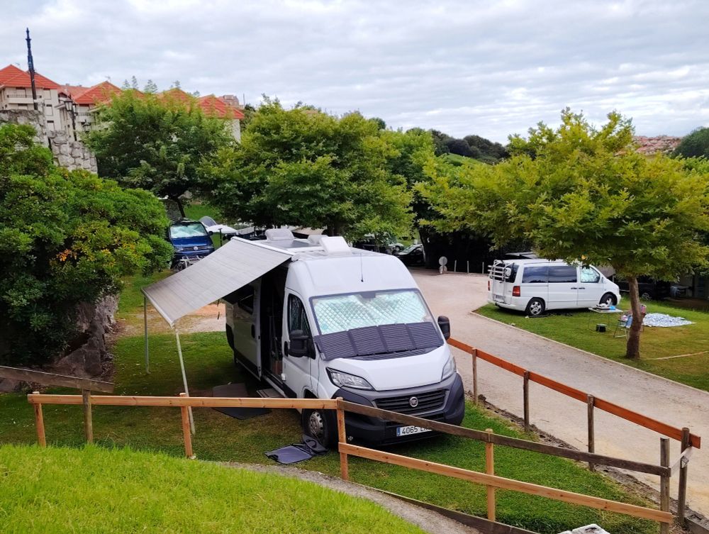 White campervan on a grassy pitch with awning extended. Gey clouds in the background. 