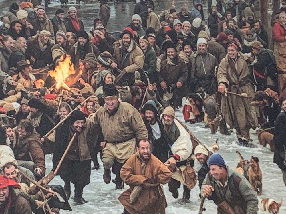 Part of mural at riverside in Kingston upon Thames above Côte Brasserie, showing medievalish-looking people, mostly men, splashing through water with sticks and odd-looking dogs, all smiling with the same kind of unearthly smile.