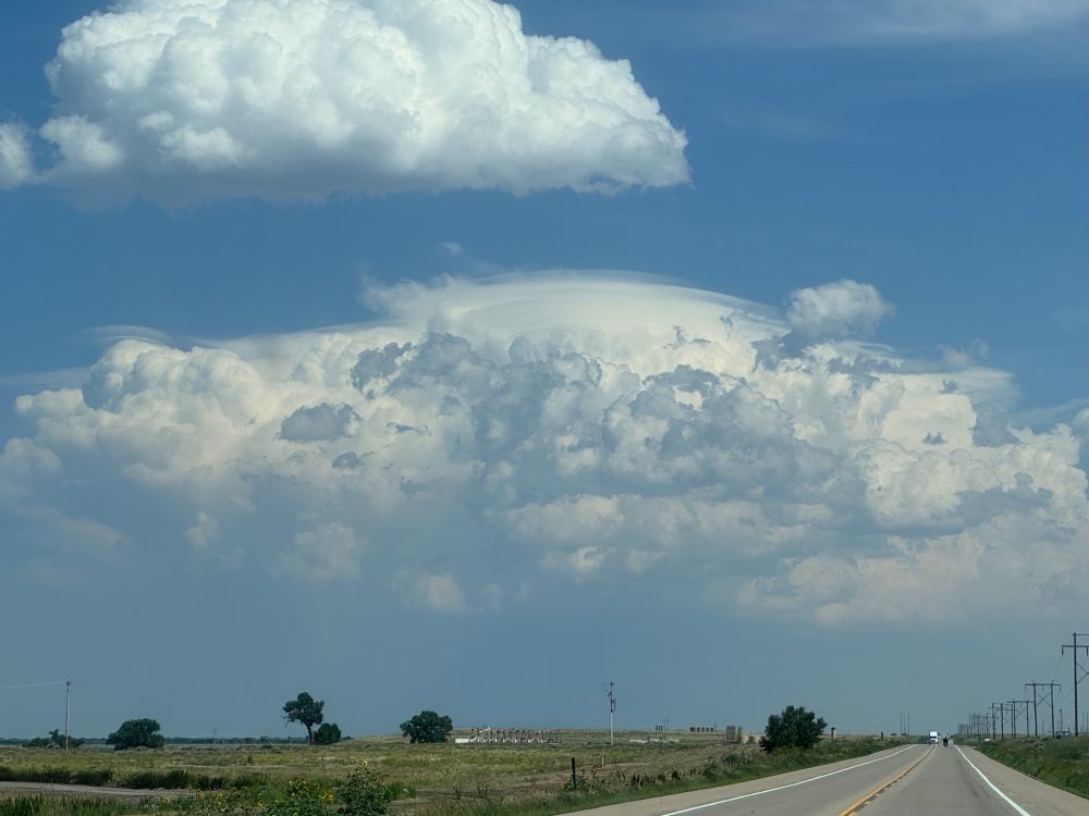 Lenticular pileus "cap" clouds over a rising storm east of Greeley, Colorado.  There is a 2 lanehighway through the high plains, still somewhat green.