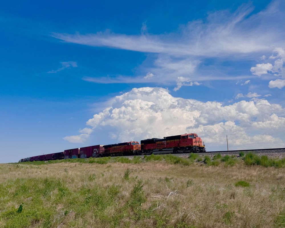 A BNSF train with a storm cloud rising up behind it.