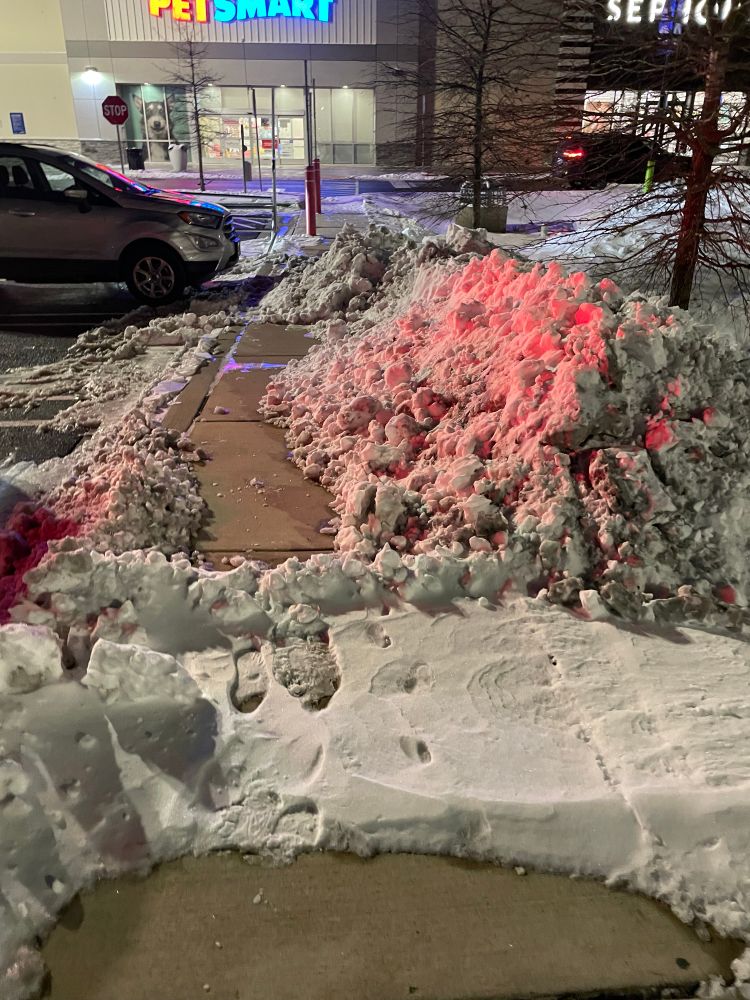 Photo showing huge pile of snow on top of sidewalk at retail center. 
