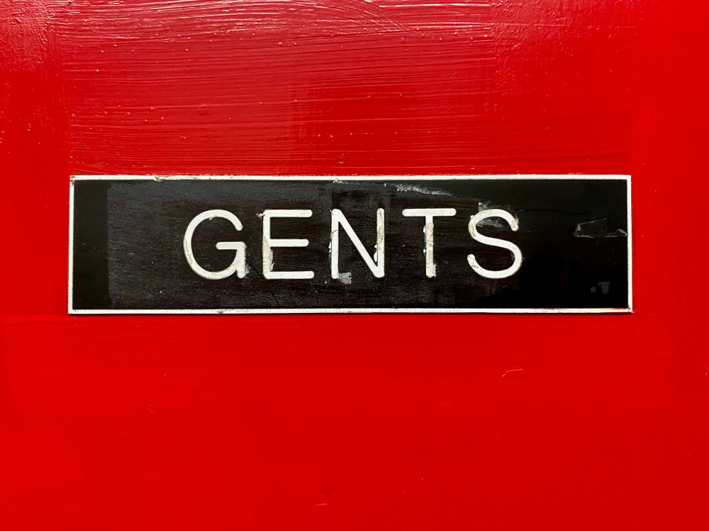 Sign on red door. ‘Gents’ in white all caps on black background. 