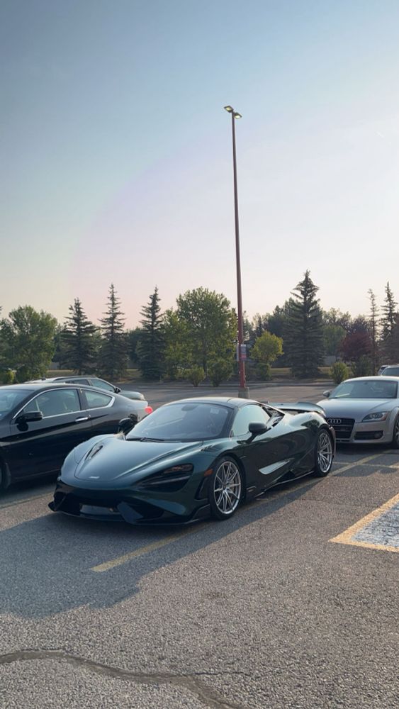 A sleek McLaren 765LT in a mesmerizing MSO “Special XP Green” shines in a sunlit parking lot, stealing the spotlight from the surrounding cars. The dramatic curves and aggressive stance make it impossible to ignore—pure automotive art in its natural habitat.