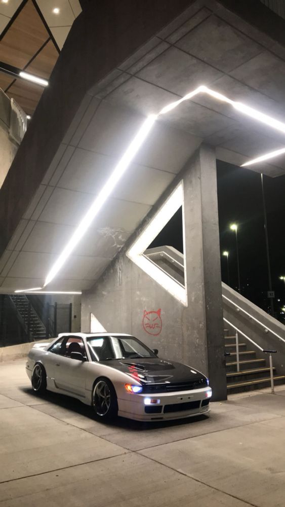 “A clean Nissan Silvia posed under modern geometric lighting, blending sleek design with urban aesthetics—capturing the essence of style and simplicity.”