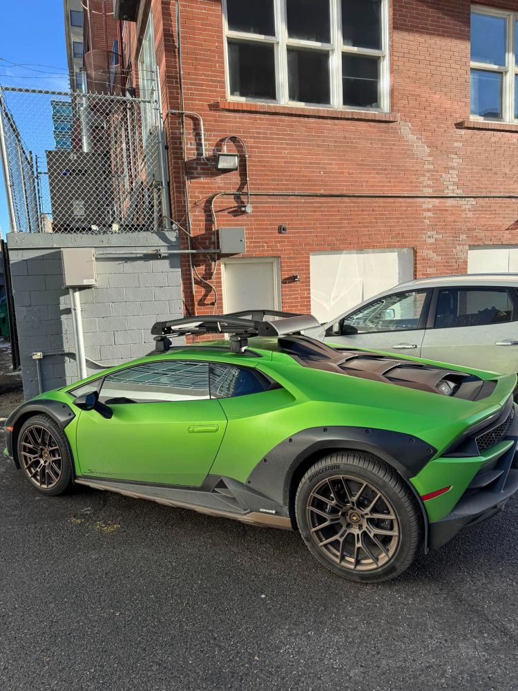 A vibrant green Lamborghini Huracán Sterrato parked in an urban setting, showcasing its rugged off-road style with flared fenders, roof rails, and a bold design