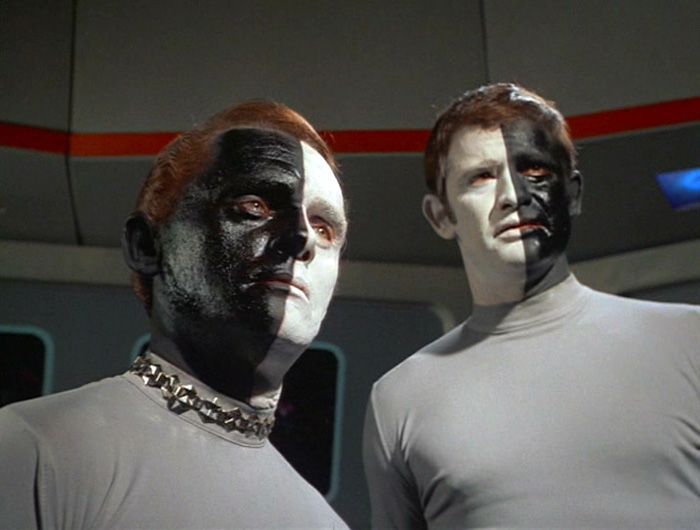A still from the Star Trek original series episode “Let That Be Your Last Battlefield” depicting Bele and Lokai, two aliens from the planet Cheron. One is white down the right side of their body and black down the other side, while the other alien is the opposite, black down the right aide and white down the other.