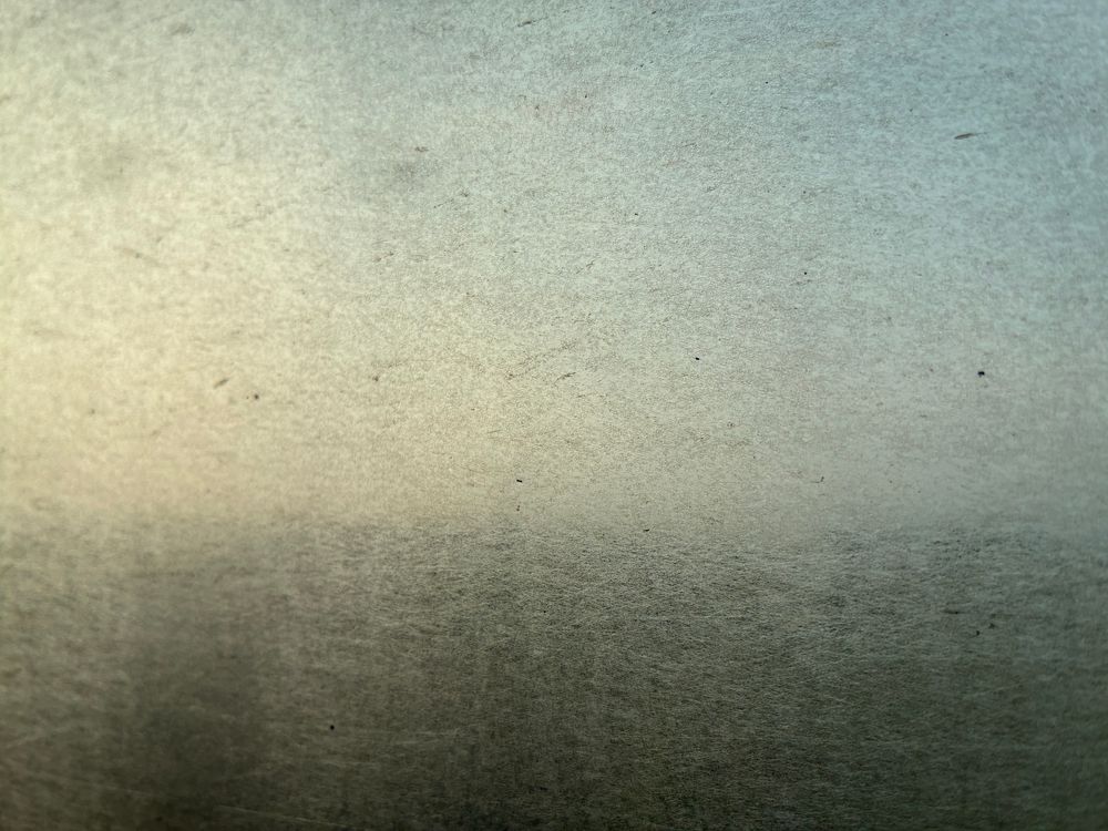Photo of a train window from inside. It's so filthy and filled with decades of micro-scratches that you only tell that the top half is light and the bottom half dark.