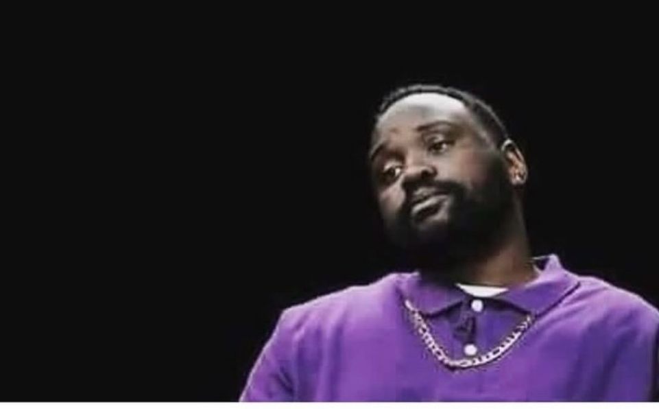 A man wearing a purple shirt and silver link chain necklace. He has an exasperated look on his face. 