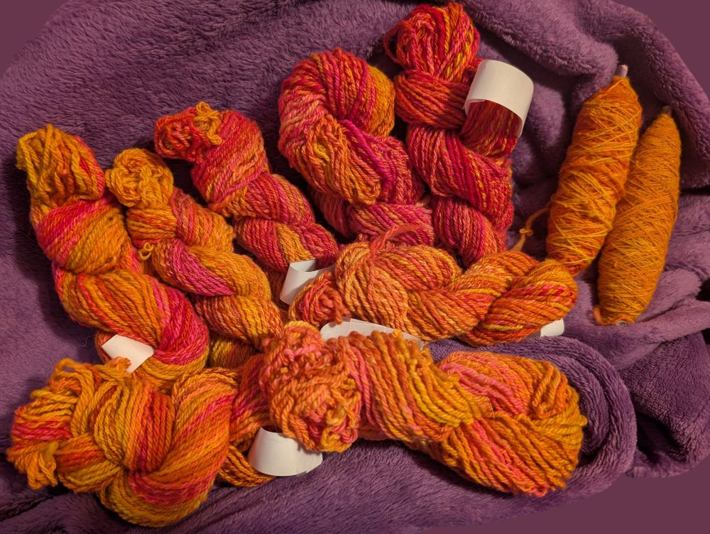 Eight skeins of chain-plied yarns in orange, red, and pink... And two quills of singles yarn