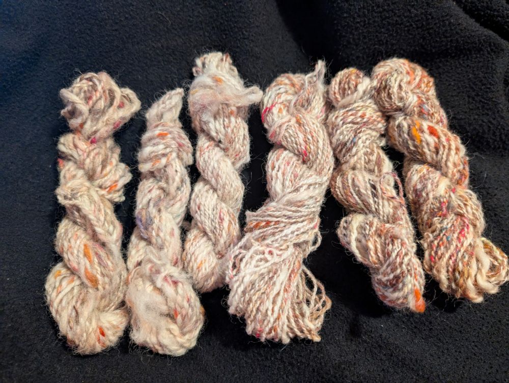 Six skeins of white yarn with tweed-like spots and flecks of orange, red, and brown