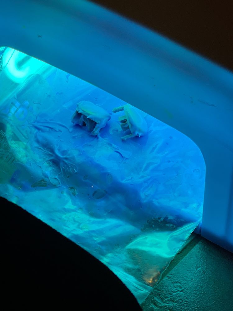 Two Dreamcast lid buttons with a makeshift retro bright schmear, under a small nail lamp