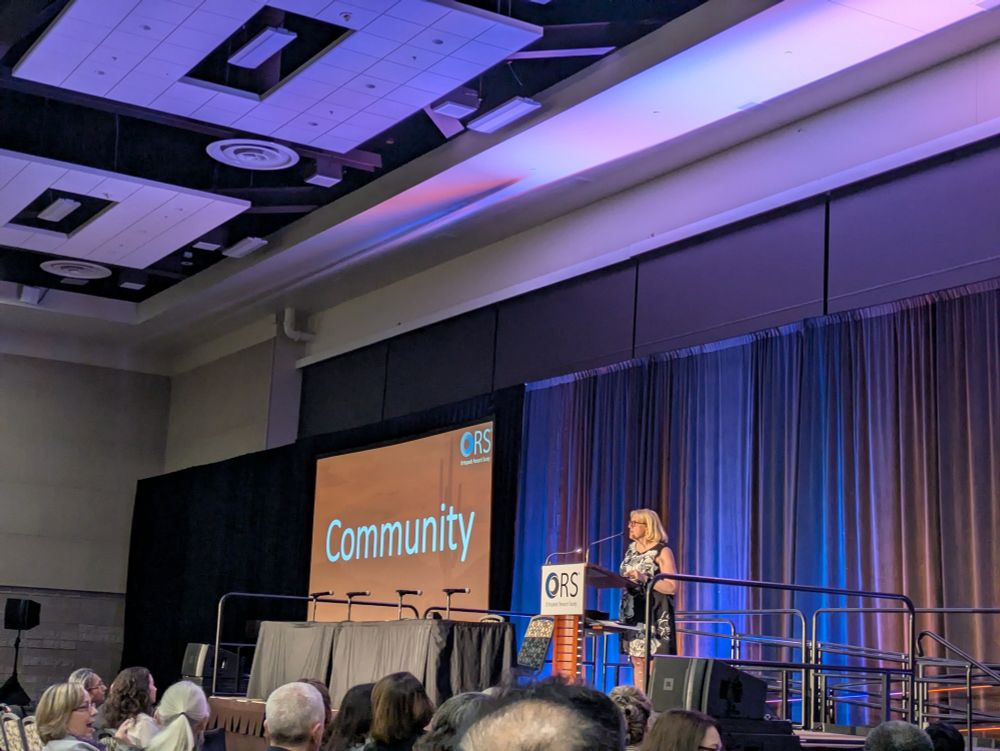 ORS President at a podium in front of a screen showing the word Community 