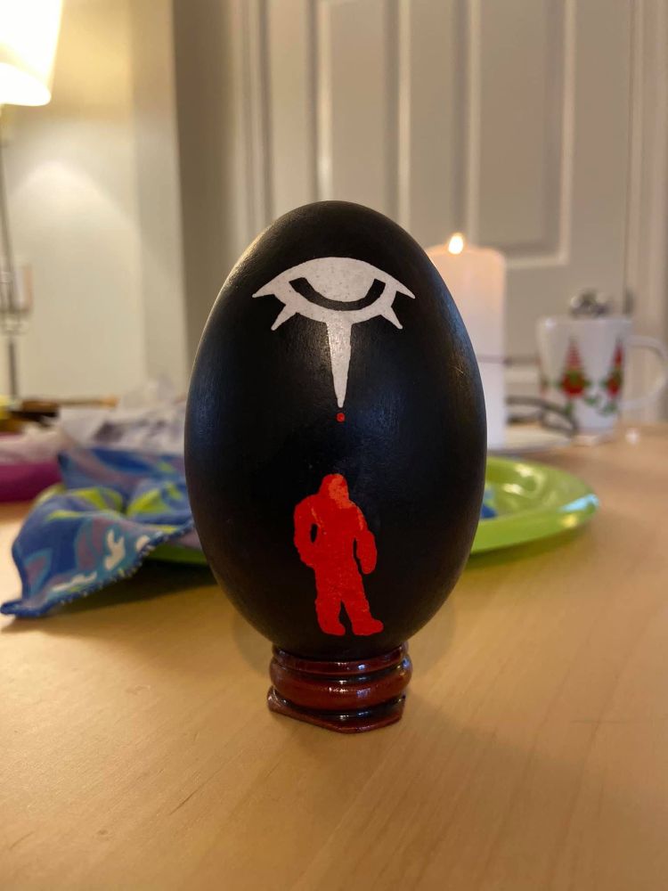 A goose egg pysanky. There’s a white eye icon above a red creepy figure.
