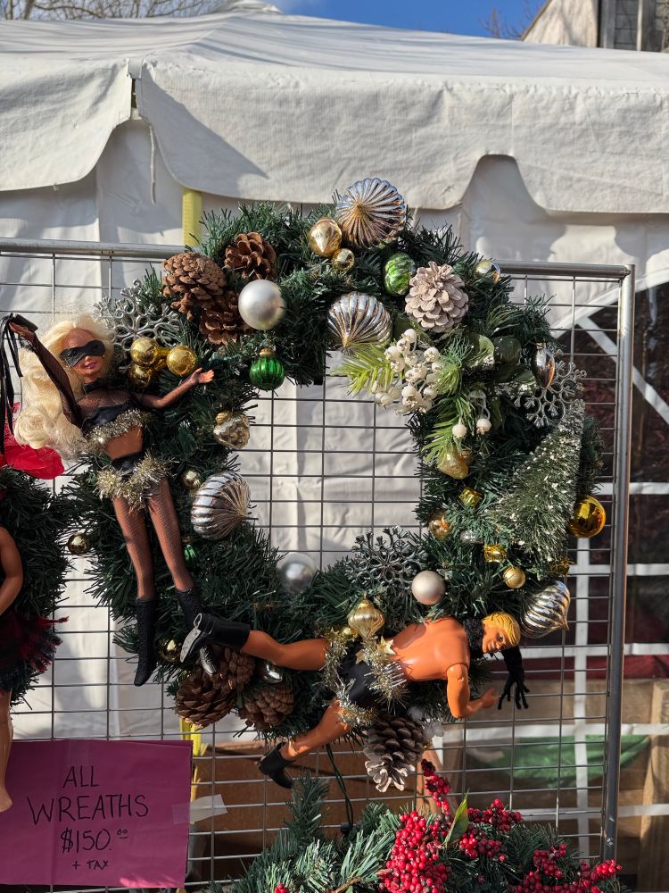 A female dominatrix whipping her client scene on a Christmas wreath with pine cones and seashells.