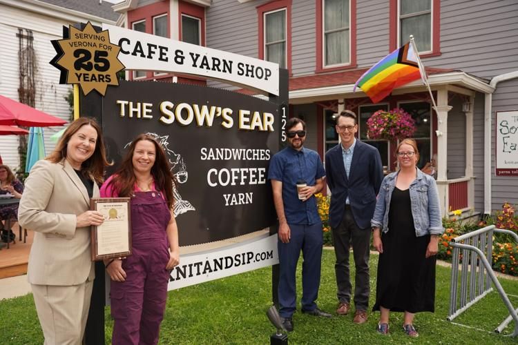 5 people pose in front of the Sow's Ear sign.  There is a Progress Pride Flag in the background. 
