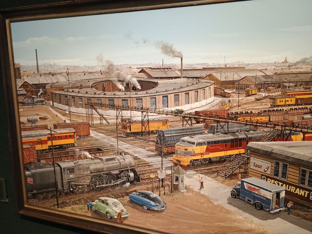 The painting A Meeting by Milwaukee Shops by Larry J. Fisher. It's features yellow locomotives by a station. 