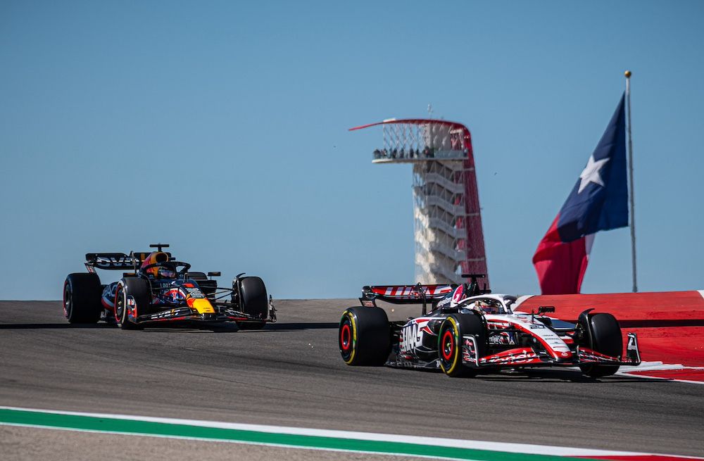 F1 vehicles racing over a small hill, with the COTA tower and a Texas flag in the background