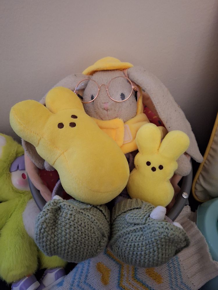 An old stuffed rabbit dressed in a yellow peep Halloween costume surrounded by tiny peep bunny plushes.