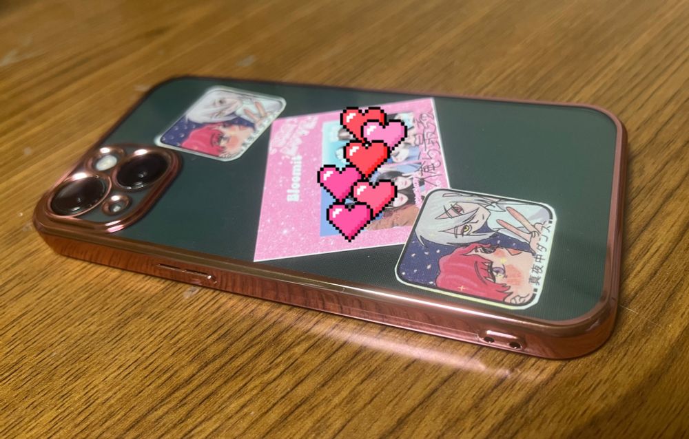 深緑色のスマホと光沢感のあるローズピンクのふちをしたクリアカバー　カバーの間に3枚のイラストや写真