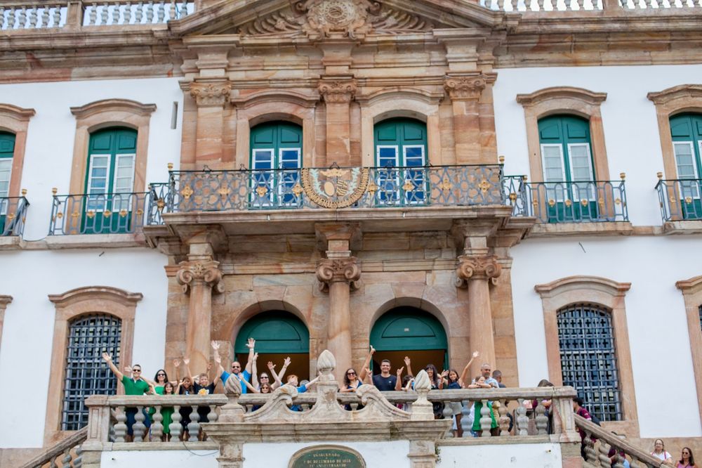 Fachada do museu em Ouro Preto com várias pessoas com os braços para cima.