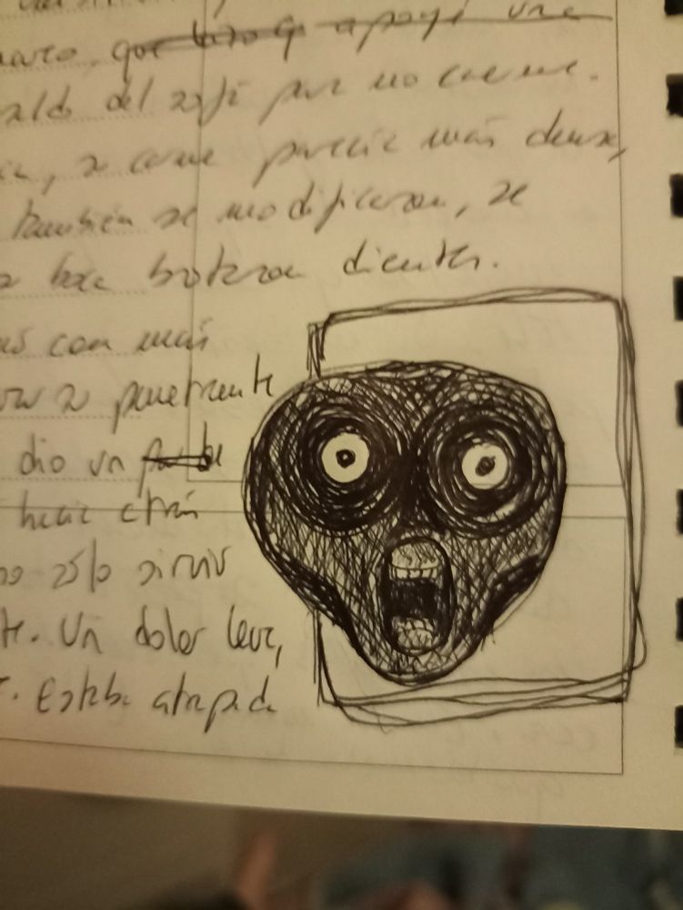 Foto de la libreta donde escribo. Entre palabras se ve un recuadro con el dibujo de un rostro oscuro, con la boca muy abierta en la que se ven  los dientes. Los ojos siguen siendo redondos.