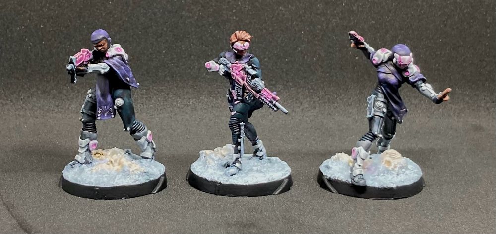 Front view of three painted miniatures in a colour scheme of dark blues and purples. Metal armor is silver white, and any lights are magenta. The two on the sides are Initiate units, and the middle is an Orphan unit - all from the Observance subfaction. They stand on moon-like basis, with dusty and partially covered old bones.