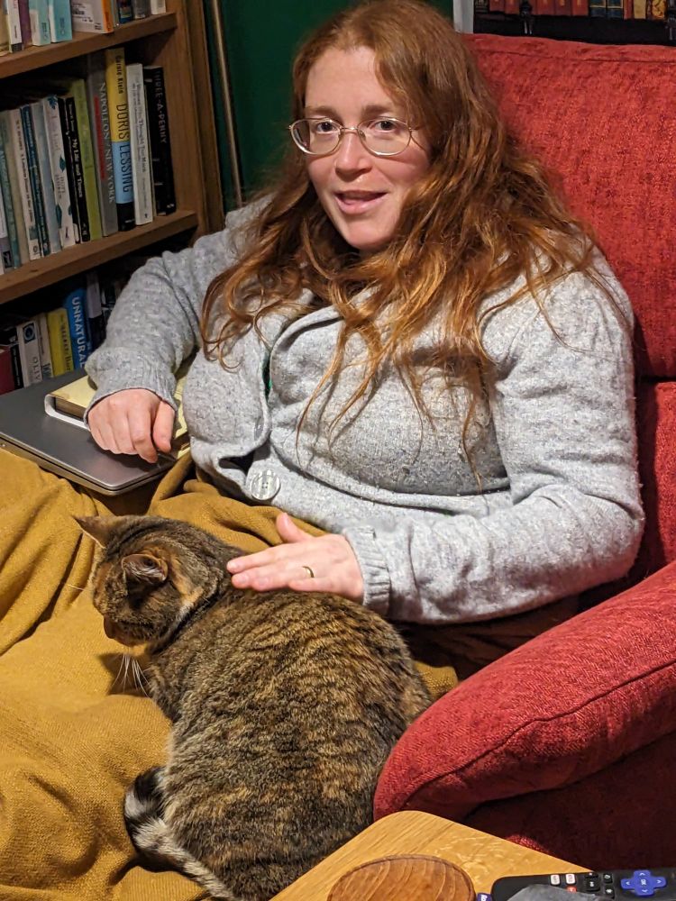 Me in an armchair under a blanket, cat half on me.